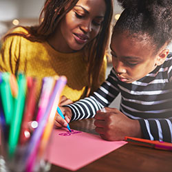 A woman and child drawing a picture together with crayons.