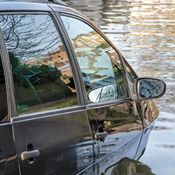 A vehicle that is stuck in flood waters with the water almost reaching its windows.