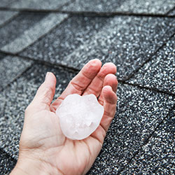 A large hailstone in a person's hand against the back drop of the home's roof.
