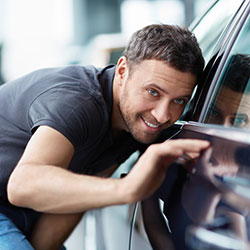 A man looking at the lines of a luxury vehicle in the dealership's showroom.