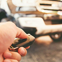 A closeup of a man's hand holding car keys and pressing the button to unlock his vehicle.