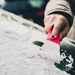 A close up of a woman's hand while she scrapes the ice off of her car's windshield.