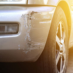 A closeup of the damage caused on a silver car's bumper from an accident.