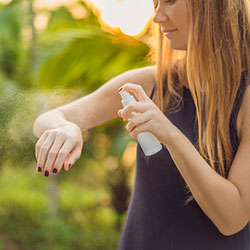 A woman spraying insect repellant on her arm.