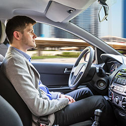 A man the wheel of a self-driving car with his hands on his lap.